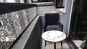 Una pequeña mesa redonda con cubierta de mármol, ubicada en un espacio exterior estrecho con una verja metálica decorativa y una silla de color oscuro.