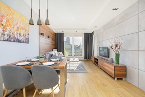 Un espace repas moderne avec une table en bois dressée pour quatre personnes, des chaises grises et un grand tableau accroché au mur.