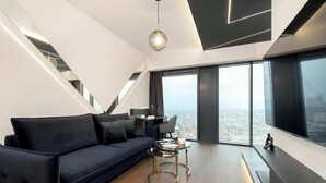 A modern living room with a dark blue sofa, a round gold table, and a large window offering a city view. - Unique Studio with a View | Parking | Jacuzzi (Katowice)