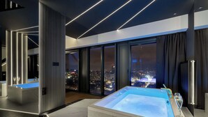 A modern bathroom with a large bathtub, a glass-enclosed shower, and a city view through large windows. - Unique Studio with a View | Parking | Jacuzzi (Katowice)
