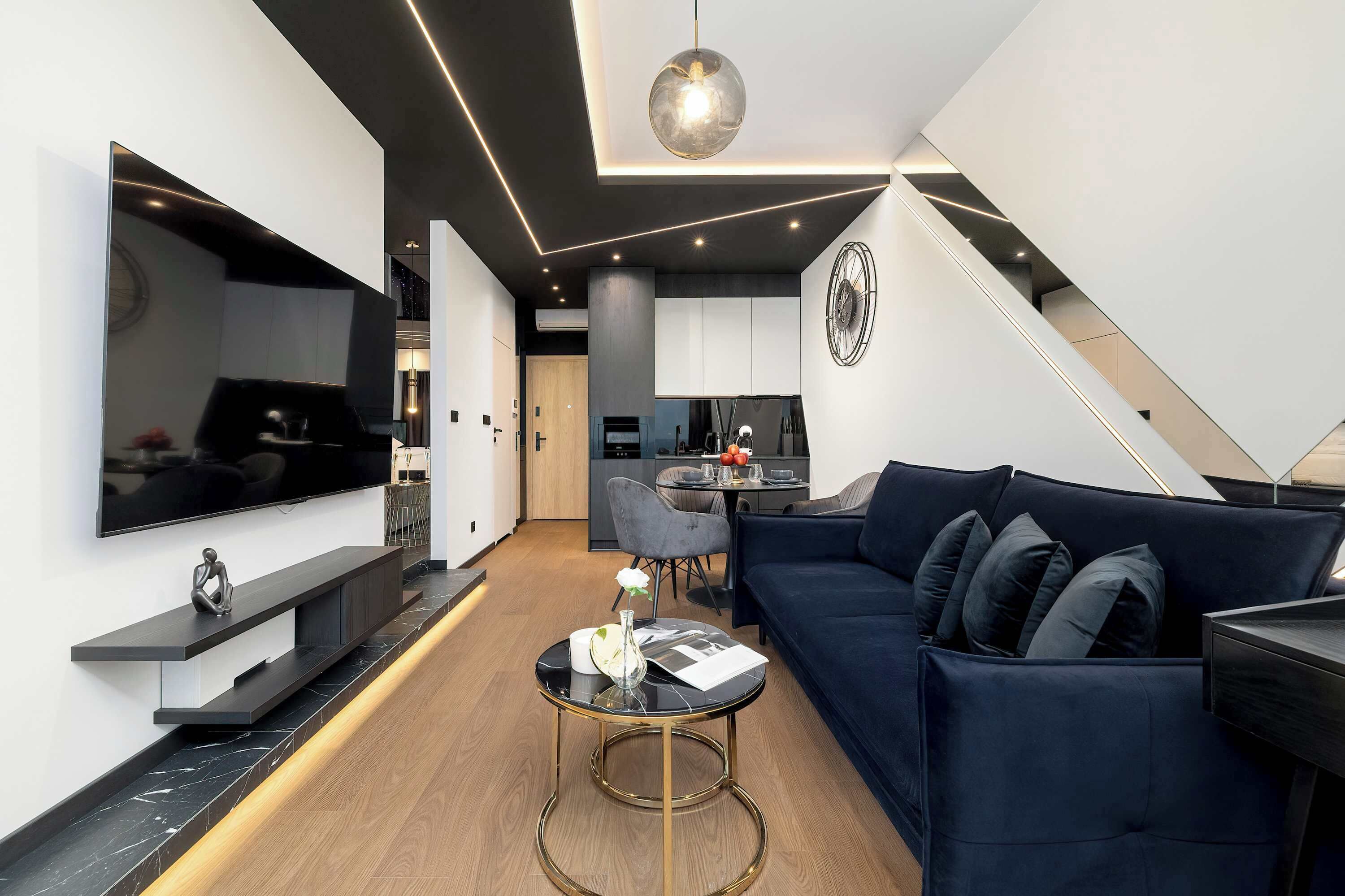 Una sala de estar moderna con un sofá azul oscuro, una mesa de centro redonda y un televisor de pantalla plana montado en la pared.