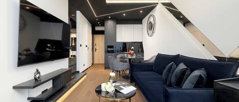 Una sala de estar moderna con un sofá azul oscuro, una mesa de centro redonda y un televisor de pantalla plana montado en la pared.