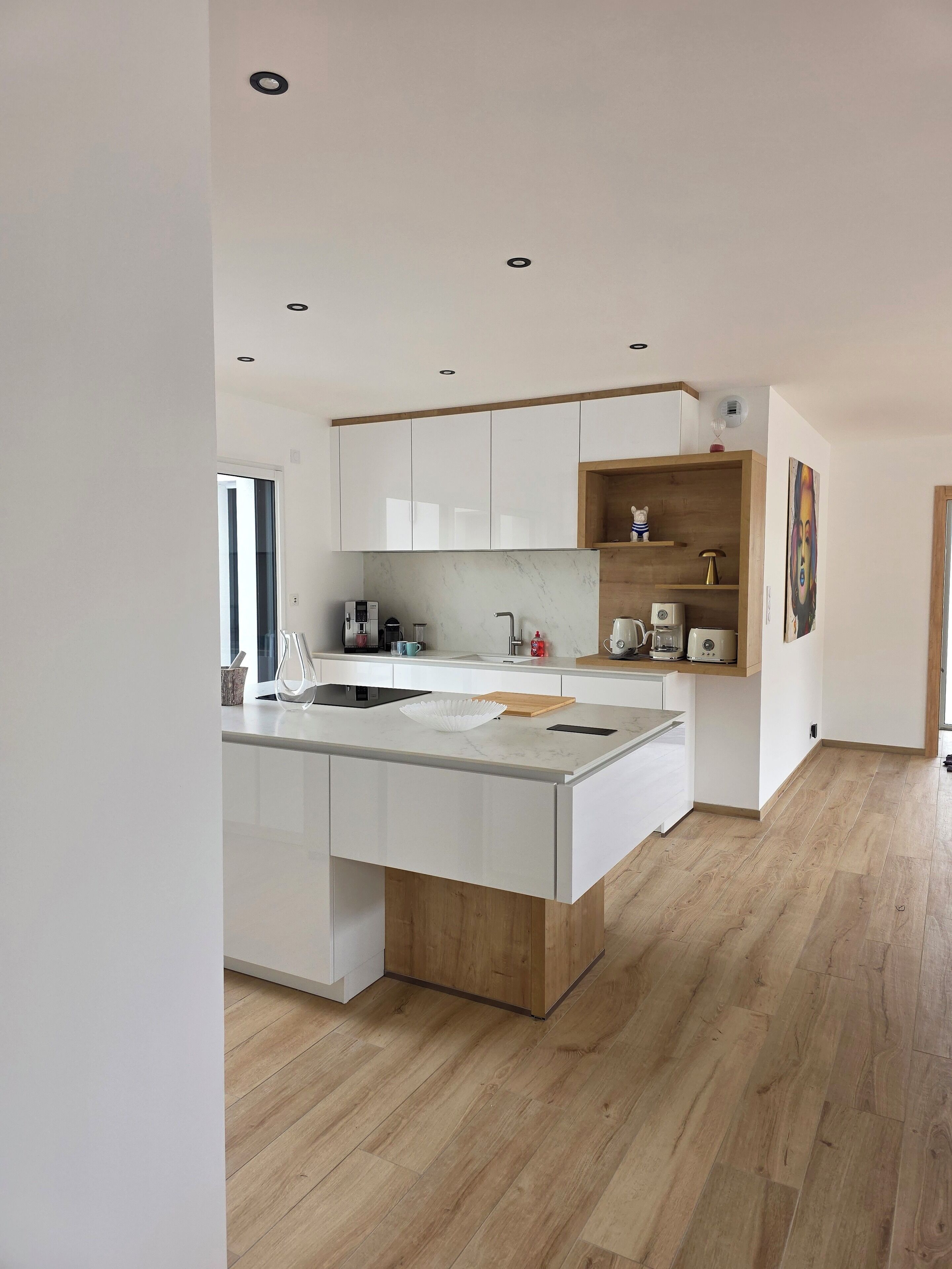 Een moderne keuken met een centraal eiland, houten kasten en een ingebouwde houten plank.