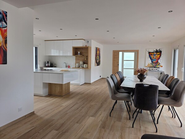 Une cuisine moderne avec des meubles blancs, un îlot central en bois et un coin repas comprenant une table en marbre et des chaises en cuir.