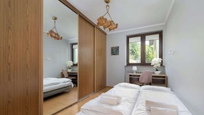 Ein Schlafzimmer mit einem großen Bett, einem Schreibtisch mit Stuhl, einem Spiegel und einem Fenster mit Blick auf Grünflächen.