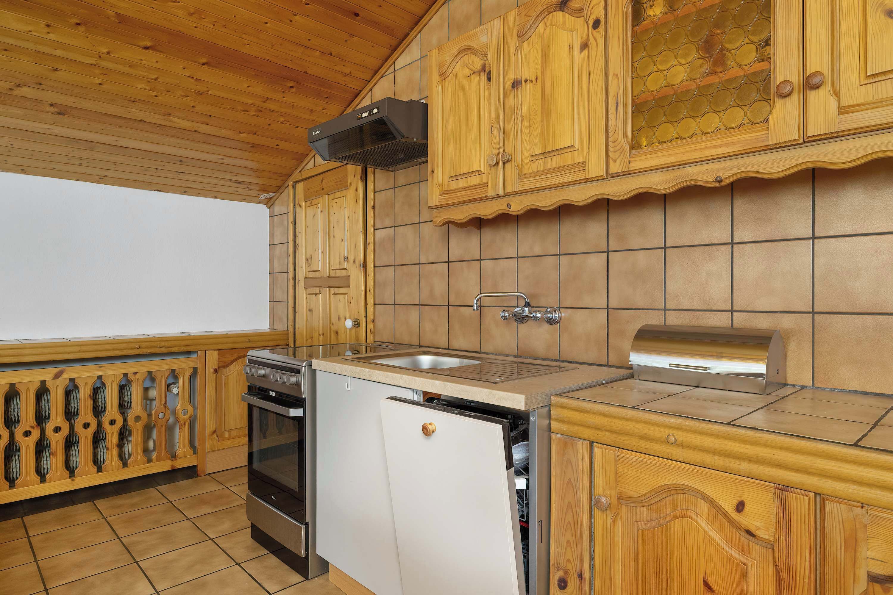 Una cocina compacta con armarios de madera, horno empotrado, lavavajillas y un lavabo.