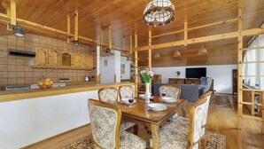 A spacious living area with a wooden ceiling, a dining table set for four, and a television in the background.