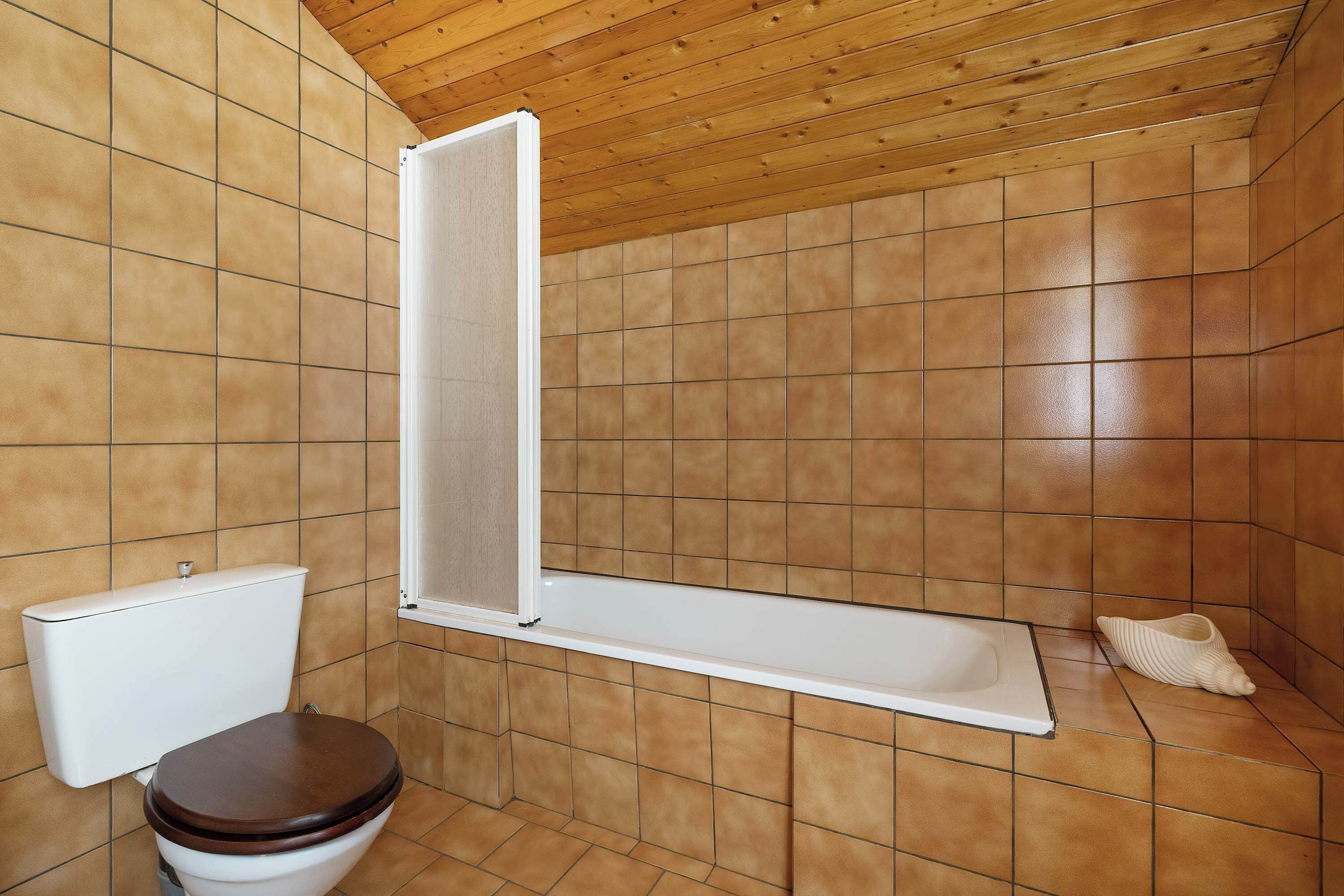 Et badeværelse med træloft, toilet og badekar.