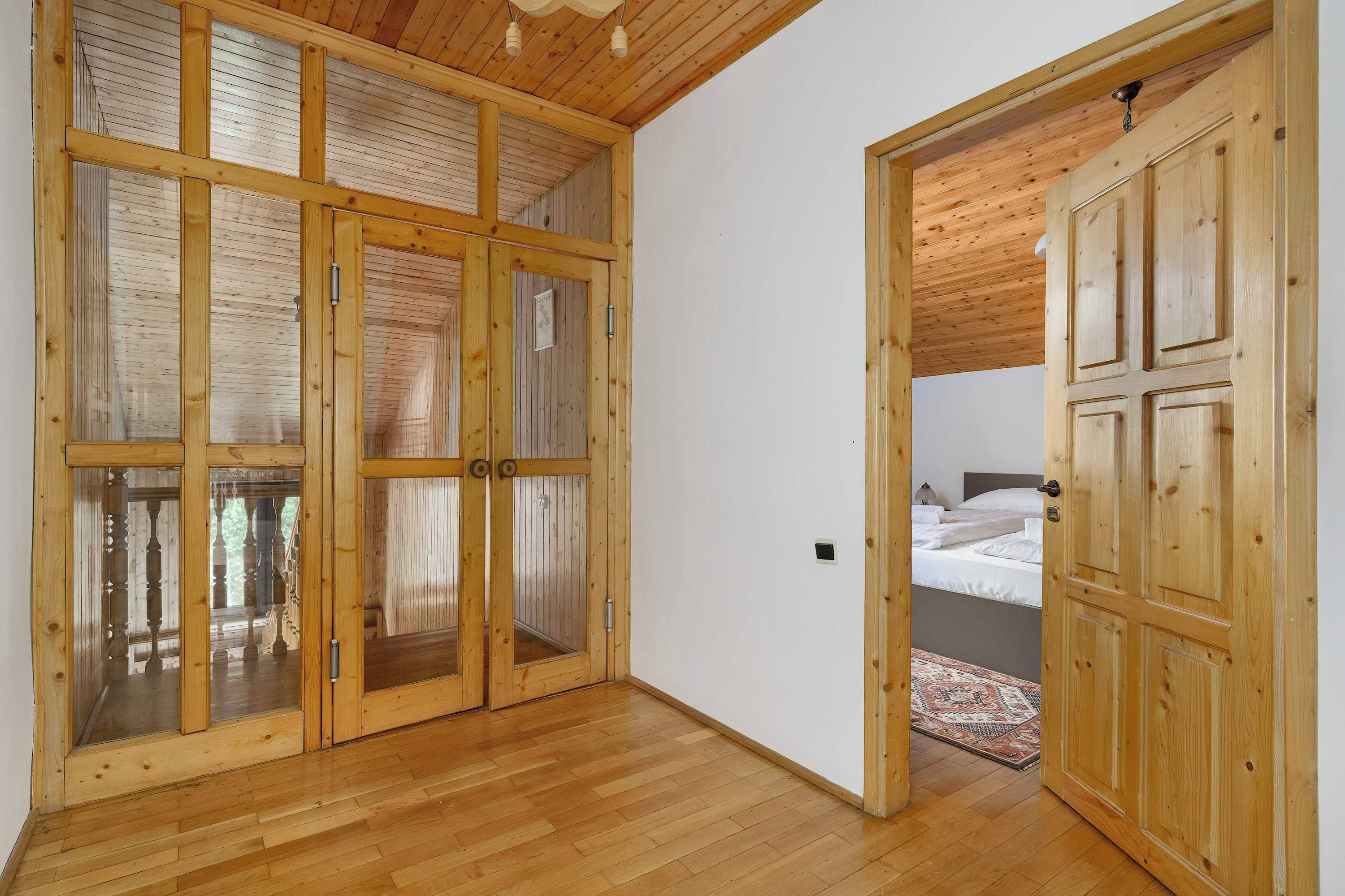 Une pièce aux murs lambrés, avec un lit, un plancher en bois et un plafond avec des poutres apparentes.