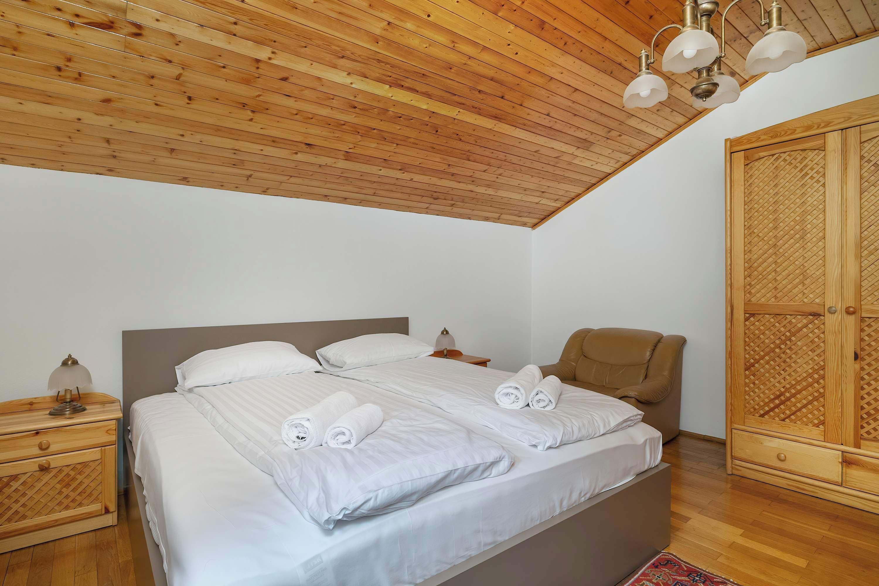Une chambre à coucher avec un plafond en bois, un lit recouvert de draps blancs, une table de chevet, une chaise et une armoire.