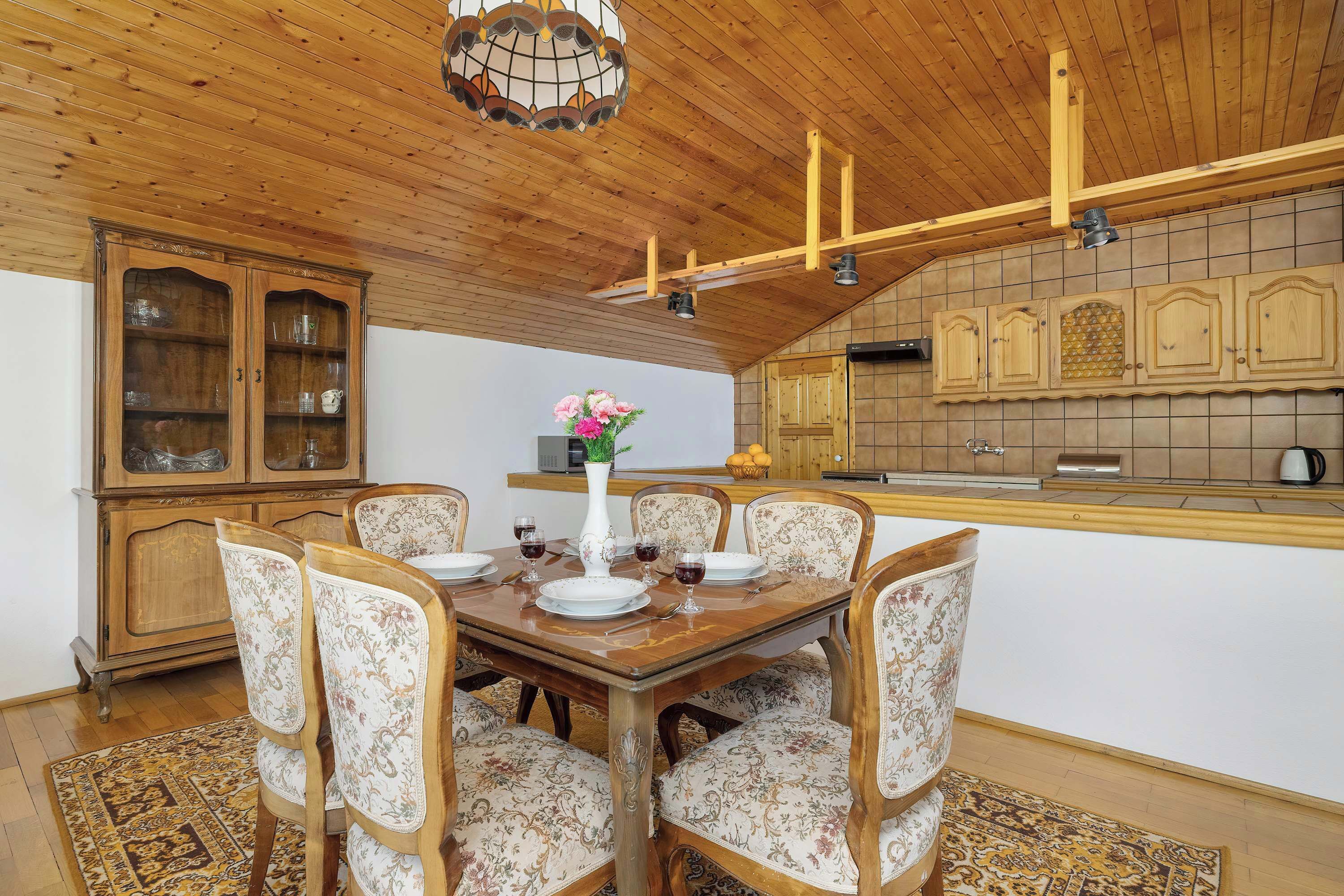 Un coin repas avec une table et des chaises en bois, un lustre et une cuisine en arrière-plan.