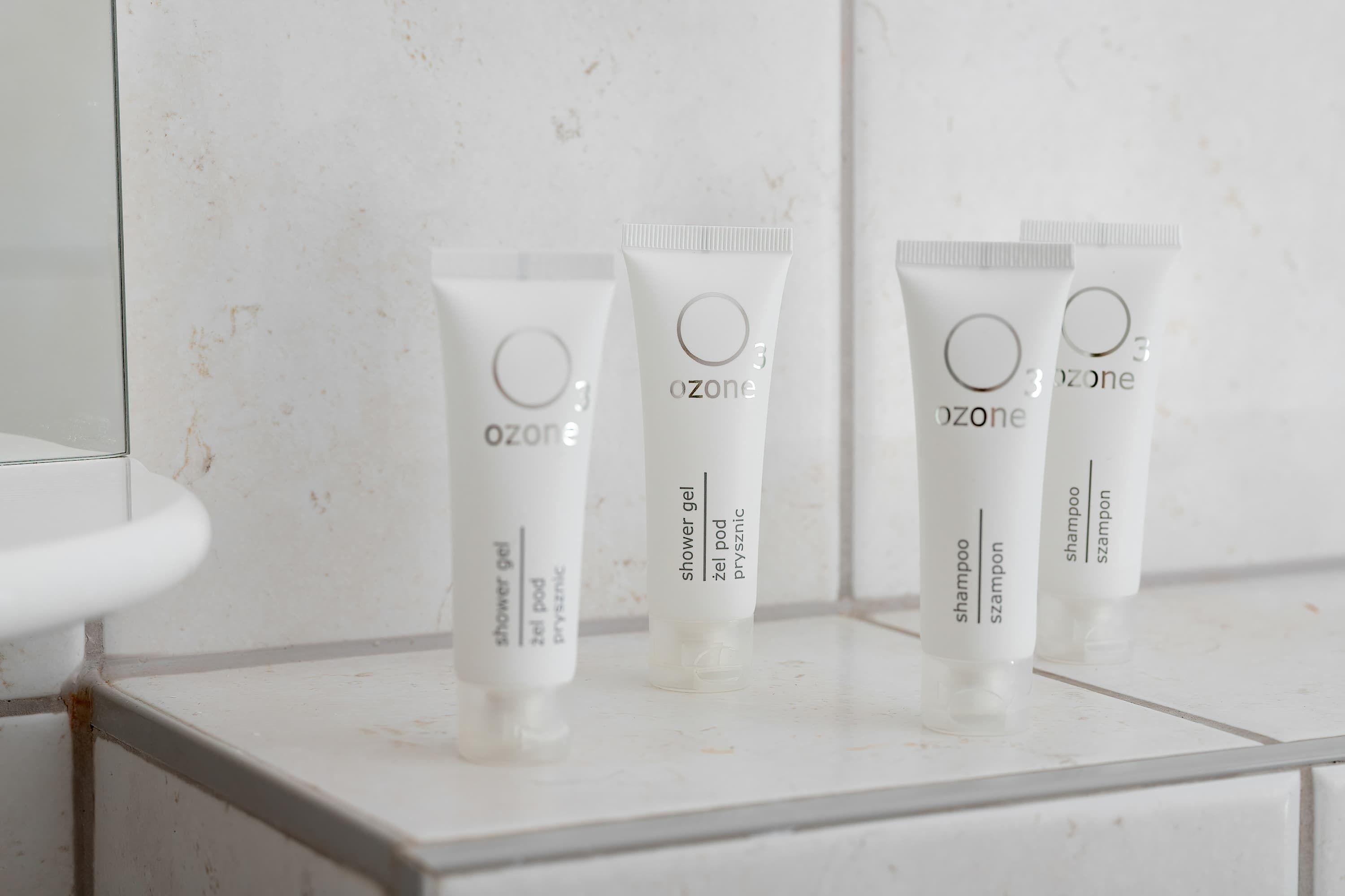 Trois tubes de gel douche Ozone blanc sont posés sur le comptoir carrelé d’une salle de bain.