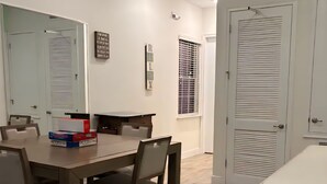 A dining area with a wooden table and chairs, a white ceiling, and a window with blinds.