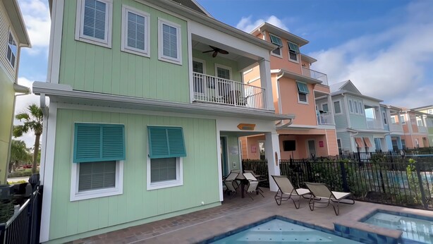 A two-story building with a balcony, a pool, and outdoor furniture.