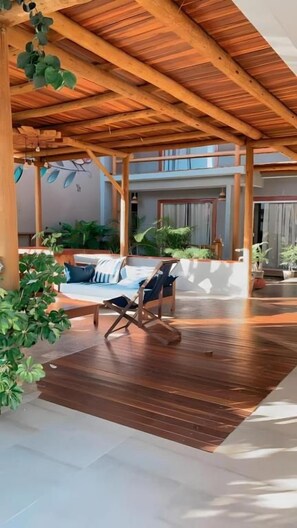 A covered outdoor area with a wooden ceiling, a lounge chair, and potted plants. - Pousada Divino Milagre (Passo de Camaragibe)