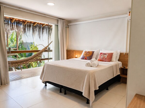 Habitación de hotel con cama, una hamaca, vistas a la vegetación y un balcón.