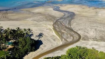 An aerial view of a beach with a winding river, dense greenery, and a clear blue sky.