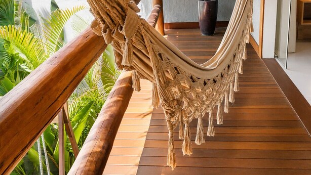 A hammock on a wooden deck with a potted plant and a door in the background. - Pousada Divino Milagre (Passo de Camaragibe)