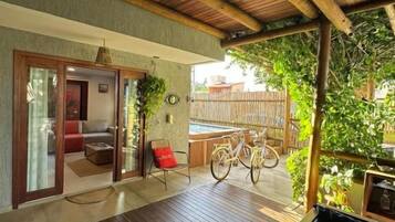 Área externa coberta com piso de madeira, um banco e uma bicicleta.