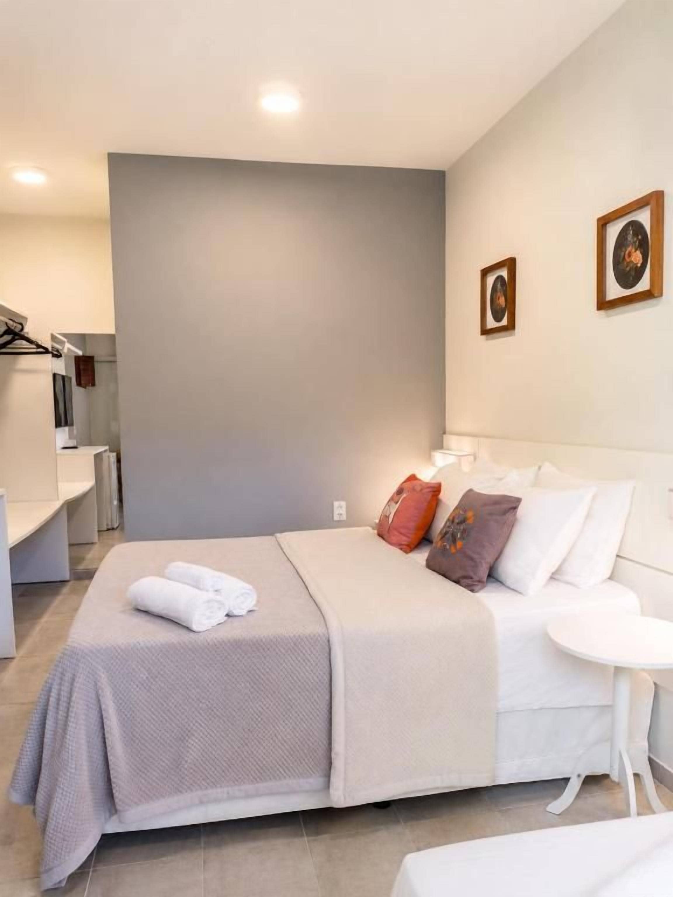 A hotel room with a bed, bedside table, and a small white table.