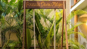 A wooden swing with a sign that reads 'Pousada Divino Milagre' in a lush garden setting. - Pousada Divino Milagre (Passo de Camaragibe)