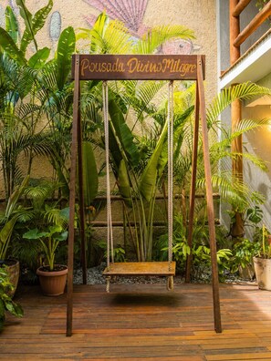 Una hamaca de madera con un letrero que dice 'Pousada Divino Milagre' en un jardín exuberante.