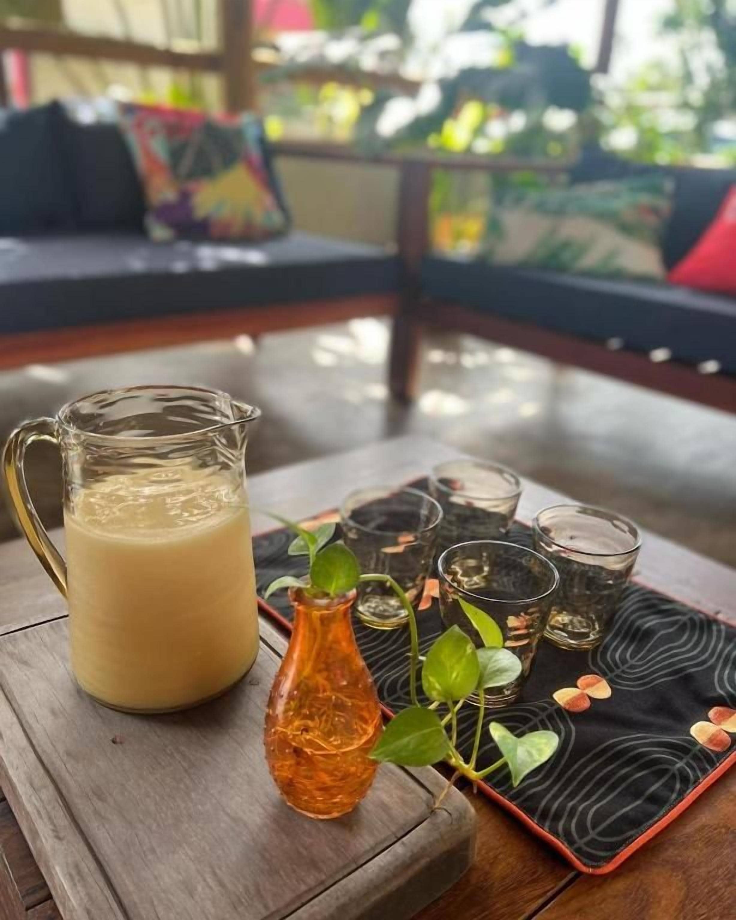 Une table en bois sur laquelle se trouvent une carafe contenant une boisson de couleur claire, une petite bouteille orange et plusieurs verres à shooter remplis d’un liquide foncé.