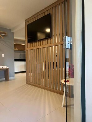 A modern hotel room with a sliding wooden partition, a flat-screen TV mounted above it, and a glass door leading to a bathroom. - Pousada Divino Milagre (Passo de Camaragibe)
