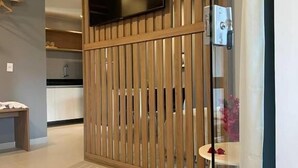 A modern hotel room with a sliding wooden partition, a flat-screen TV mounted above it, and a glass door leading to a bathroom. - Pousada Divino Milagre (Passo de Camaragibe)