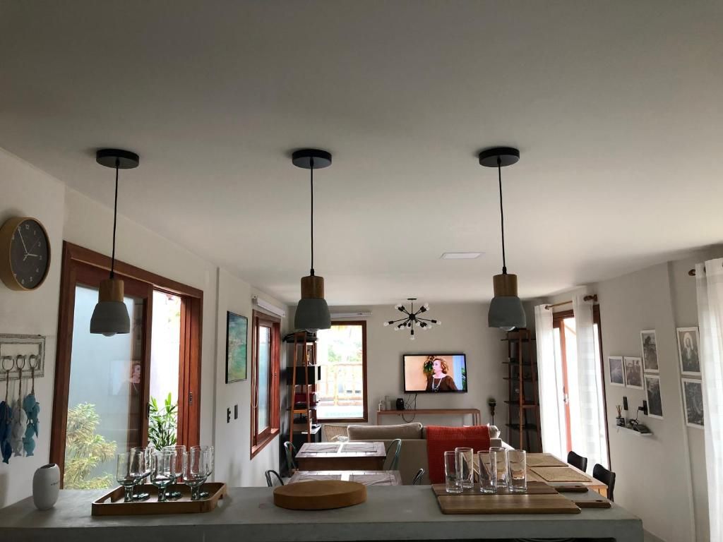 Uma cozinha moderna com luminárias pendentes, uma área de jantar com uma mesa comprida e uma televisão na parede.