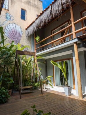 Una terraza de madera con un columpio, un balcón con techo de paja y un mural de una concha.