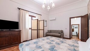 A bedroom with a bed, a television, a sofa, a wardrobe, and a door leading to another room. - GuestHost - La Maison Real Palermo (Palermo)