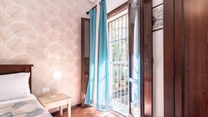 A bedroom with a bed, nightstand, lamp, and a view through a window with curtains. - GuestHost - La Maison Real Palermo (Palermo)