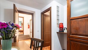 A dining area with a wooden table, chairs, a vase of flowers, and a kitchen area with a coffee maker. - GuestHost - La Maison Real Palermo (Palermo)