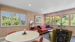 Ein modernes Wohnzimmer mit einem runden Esstisch, roten und grünen Stühlen, einem roten Sofa und einem großen Fenster mit Blick auf Bäume.