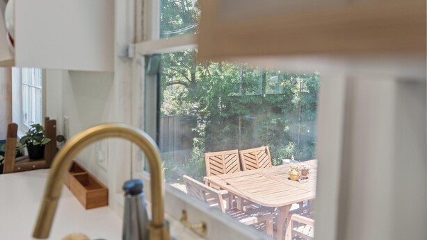 Eine Küche mit einem Fenster, das auf einen Holzesstisch und Stühle draußen blickt.