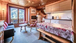 Een houten hutje met een bed, een eettafel, een bank, een televisie en een keukenhoek.