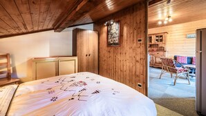 Een houten interieur met een bed, een houten kledingkast, en een zithoek met een stoel en tafel.
