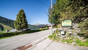 Een weg die leidt naar een chalet genaamd 'Chalet Arnica', met een stenen muur en een bordje.