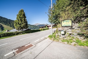 A road leading to a chalet named 'Chalet Arnica' with a stone wall and a signboard.