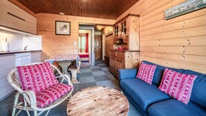 Een knus houten interieur met een eethoek, een bank met gestreepte kussens, en een houten plafond.