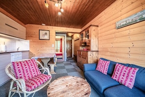 A cozy cabin interior with a dining area, a sofa with patterned cushions, and a wooden ceiling.