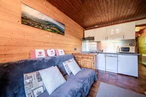 Ein gemütliches Zimmer mit einer Couch, einem Gemälde und einer Küchenzeile mit weißen Schränken und einer Mikrowelle.