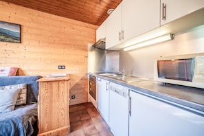 Eine kleine Küche mit Holzwänden, weißen Schränken, einem eingebauten Backofen und einer Mikrowelle.