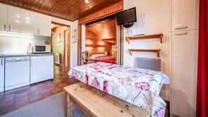 Een compacte kamer met een bed, een kleine kitchenette, een televisie en een houten plafond.