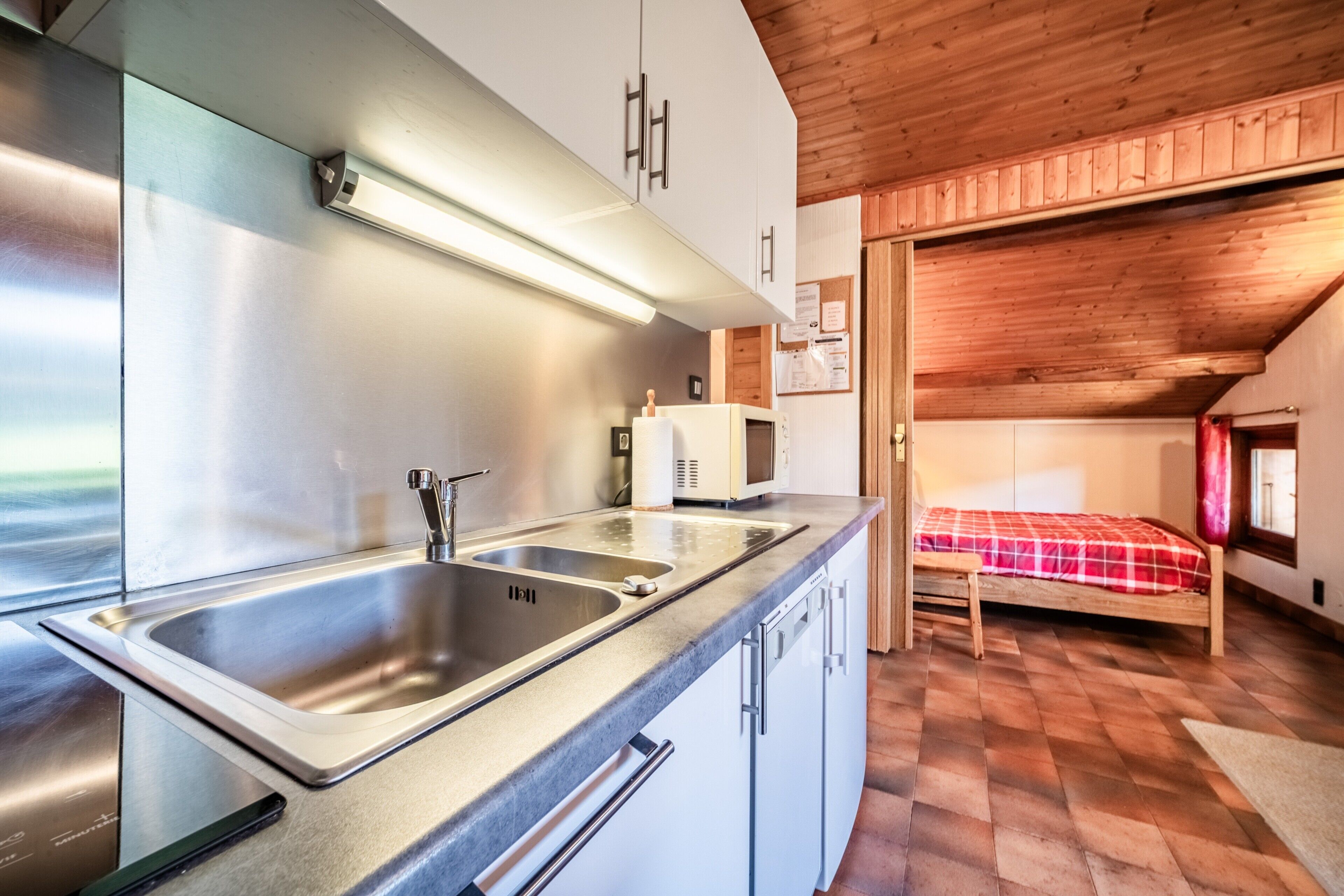 Cocina compacta con electrodomésticos de acero inoxidable, un lavamanos y techo de madera.