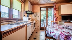 A kitchen with wooden cabinets, a sink, a microwave, and a dining table with a quilt. - Apartment 'D'arnica' with Mountain View, Balcony and Wi-Fi (Morzine)