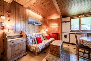 L’intérieur chaleureux d’un chalet, avec un revêtement mural en bois, un canapé, une table à manger et un lave-linge.