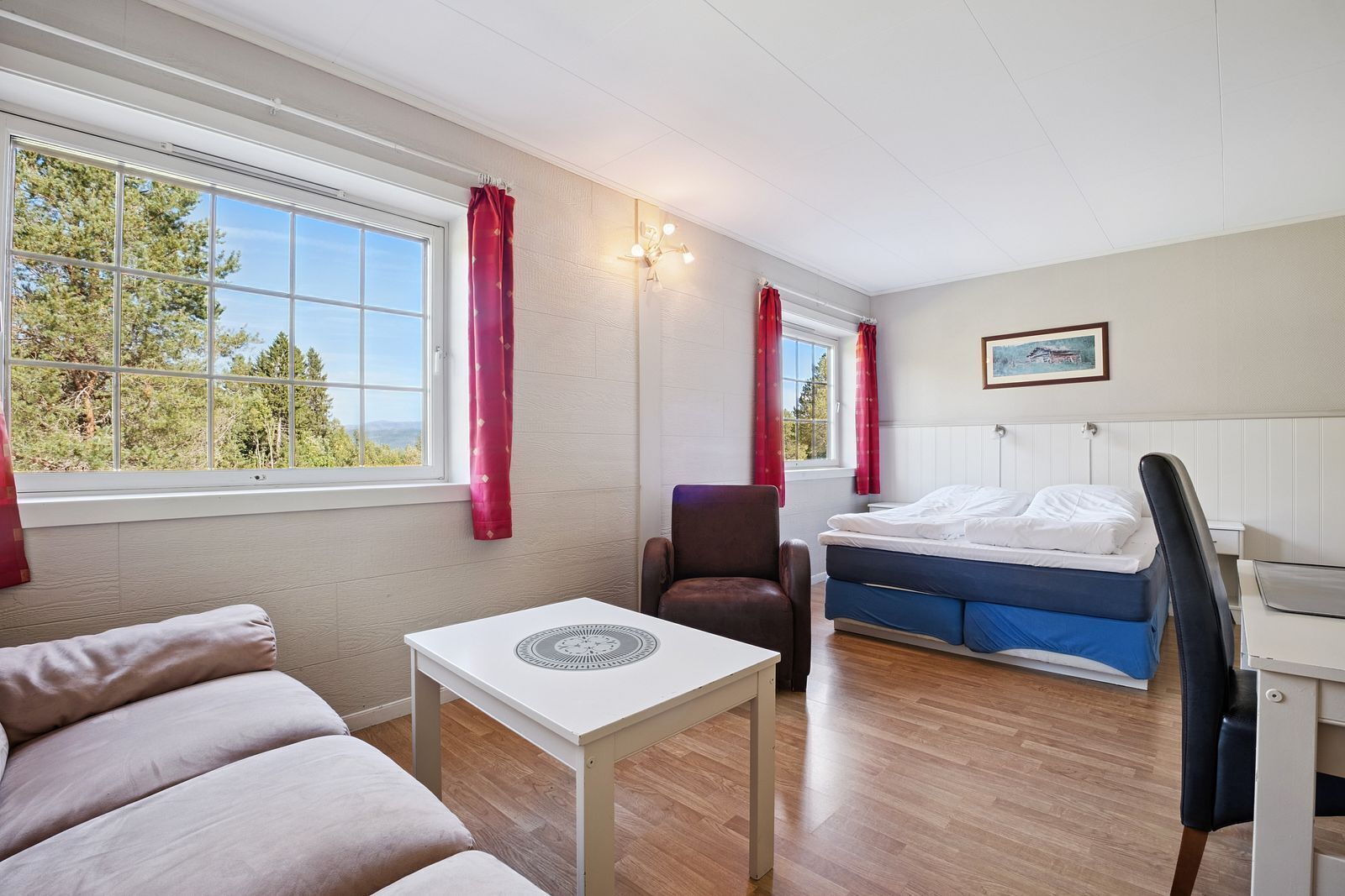 A cozy room with a bed, a chair, a table, and a window with curtains.