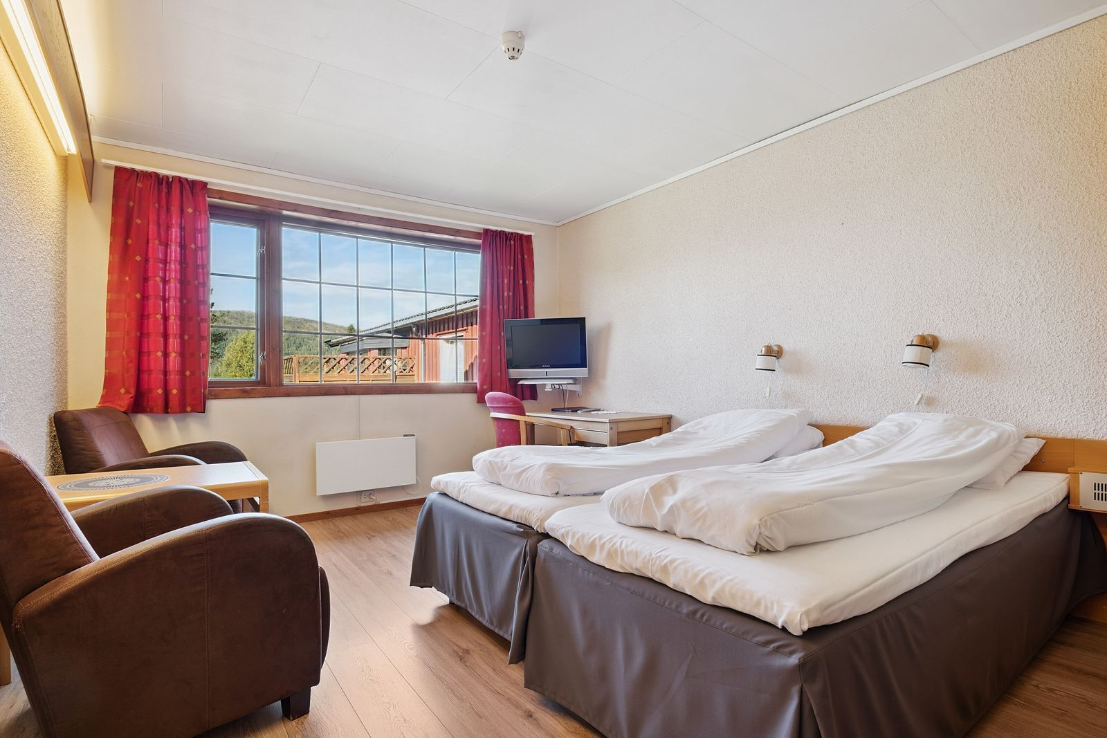 A hotel room with two beds, a desk, a chair, a TV, and a window with curtains.